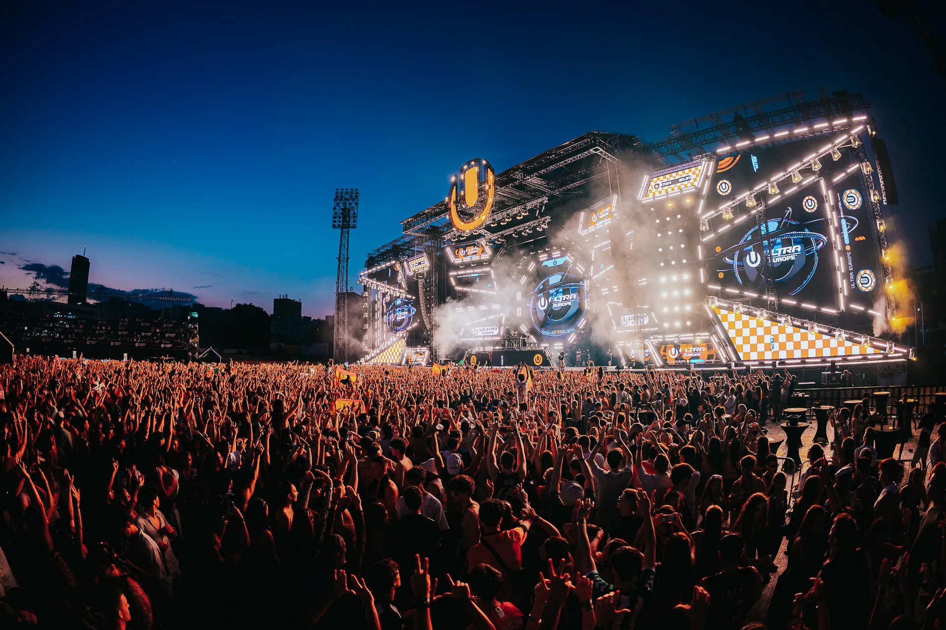 Large festival crowd in front of a brightly lit main stage at night